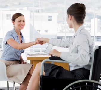 A woman in a wheelchair shaking hands with another woman.