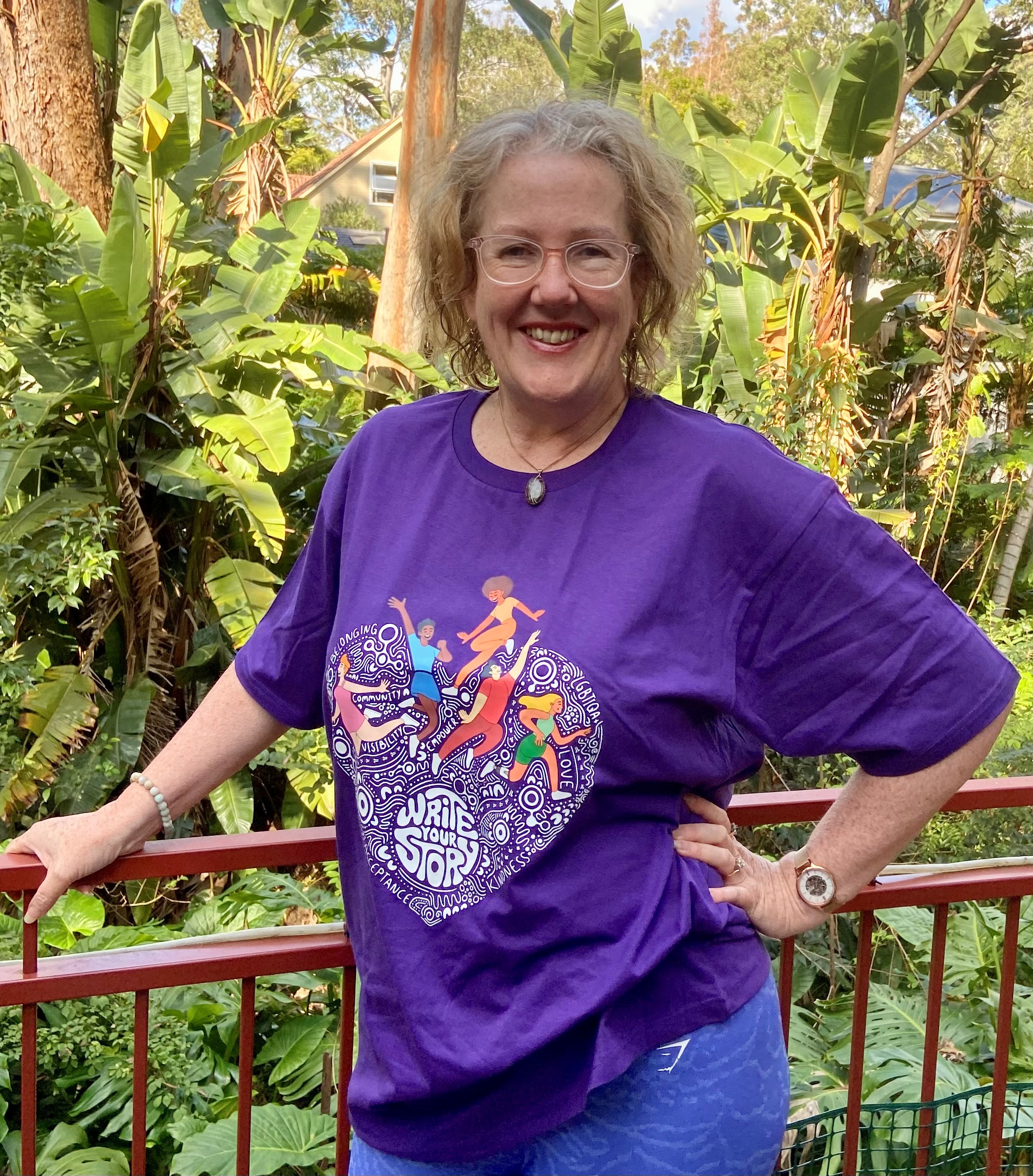 Woman standing on balcony with a rainforest view, wearing a tshirt that says "wear it purple"