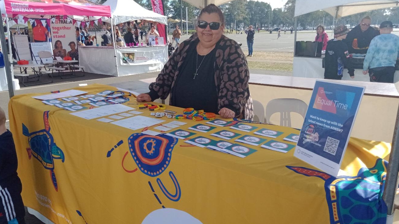 Women sitting at table behind ADNSW branded signs and merchandise