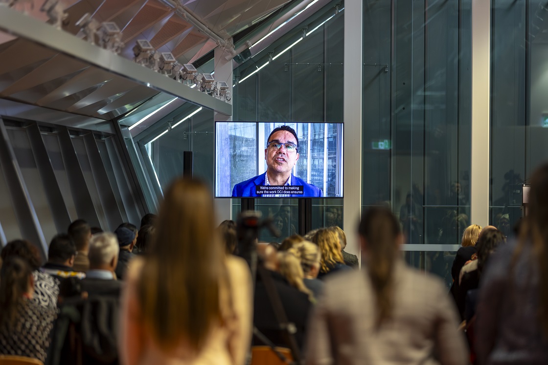 Man addressing the audience via a video on a tv screen
