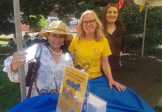 3 women standing at a stall, looking at camera smiling